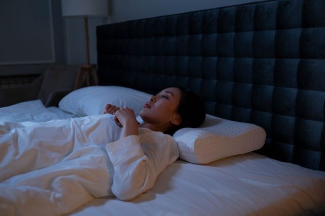 夜晚卧室里,一位成年人躺在床上,床头闹钟显示凌晨三点,窗外月光透进房间,表现半夜醒来和睡眠质量下降的场景。 夜晚卧室里,一位成年人躺在床上,床头闹钟显示凌晨三点,窗外月光透进房间,表现半夜醒来和睡眠质量下降的场景。